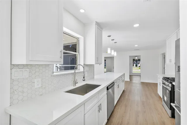 a large white kitchen with a sink and dishwasher a stove with wooden floor
