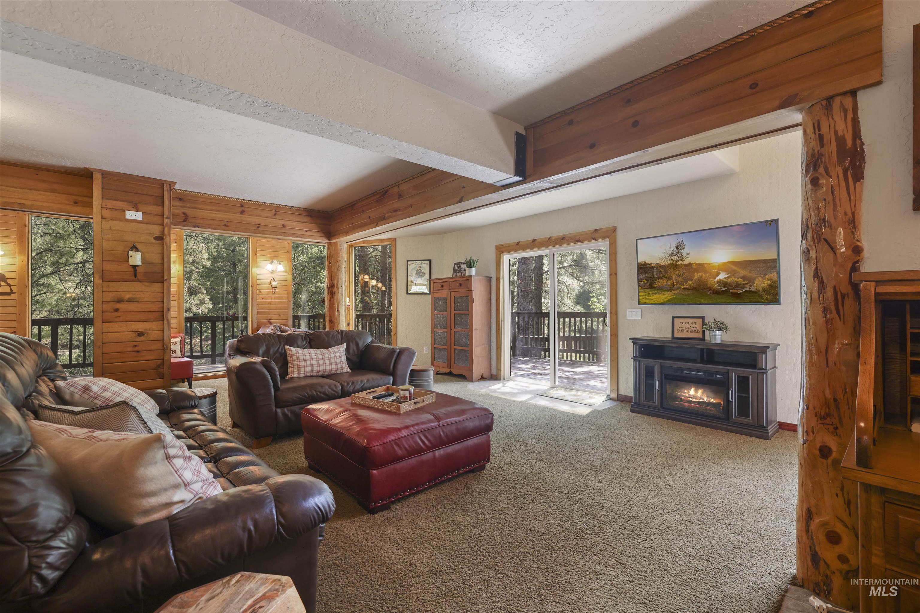 224 Dakota Road Mountain Home, ID 83647 - Photo 3 of 50 Spacious living area featuring wood-paneled walls, exposed wood beams, and a built-in media console with an electric fireplace