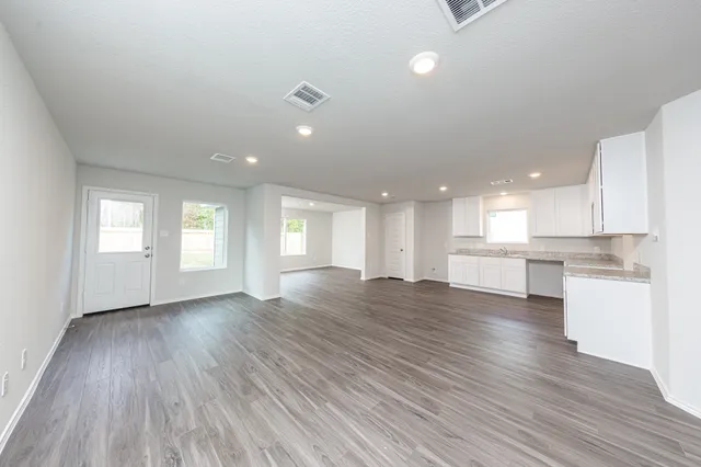 a view of an empty room and kitchen with wooden floor