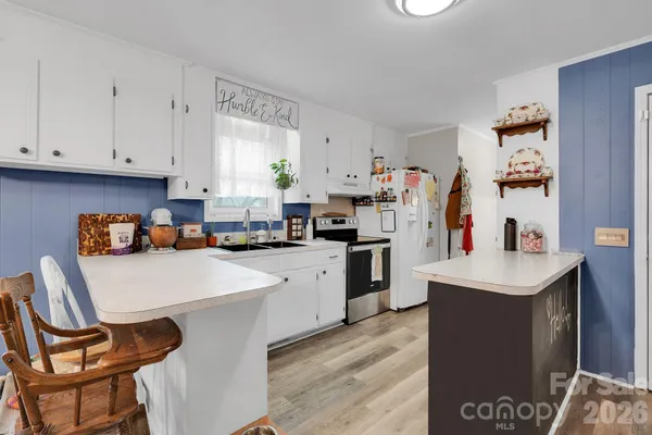 a kitchen with stainless steel appliances a stove a sink and white cabinets with wooden floor