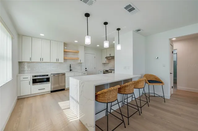 a kitchen with stainless steel appliances a stove a sink a refrigerator a dining table and chairs with wooden floor