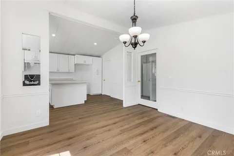 a view of an empty room and kitchen with wooden floor