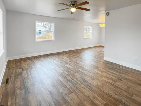 an empty room with wooden floor fan and windows