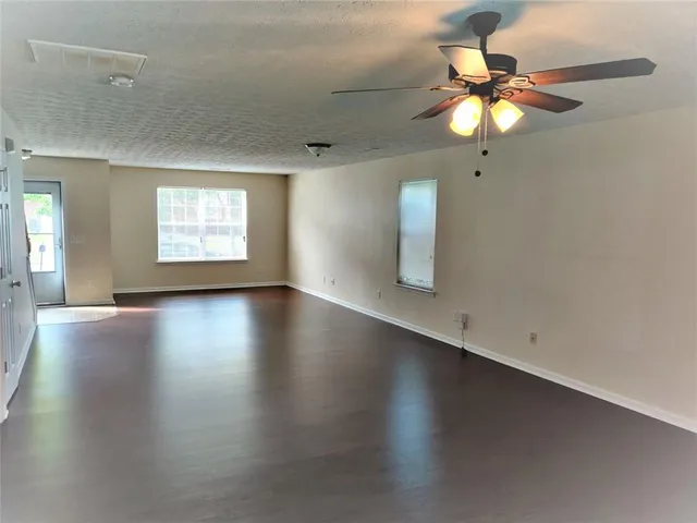 an empty room with wooden floor fan and windows