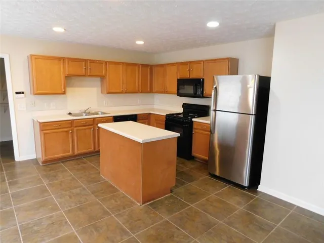 a kitchen with stainless steel appliances granite countertop a refrigerator a sink a stove top oven and cabinets