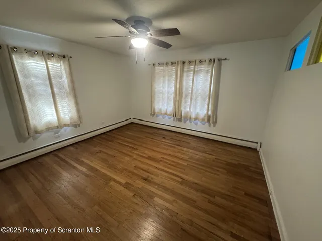 an empty room with wooden floor fan and windows