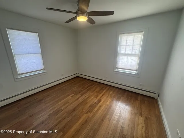 an empty room with wooden floor chandelier fan and windows