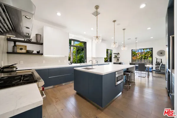 a kitchen with stainless steel appliances a stove a sink a refrigerator a center island and a wooden floor