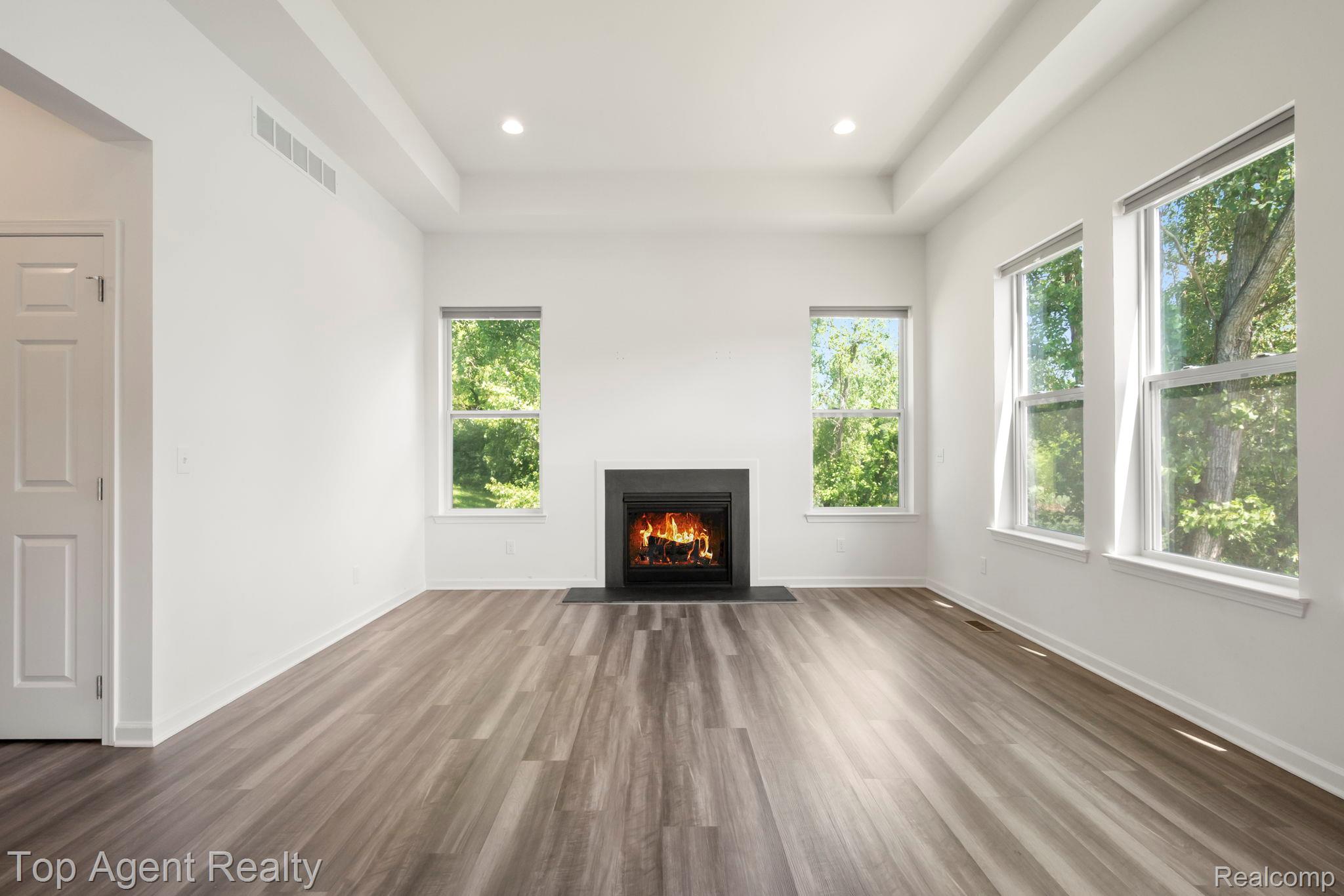 63770 Dequindre Road Washington, MI 48095 - Photo 9 of 61 Spacious living area featuring a modern fireplace with a black surround, wood-finish flooring, a tray ceiling with recessed lighting, and multiple large windows