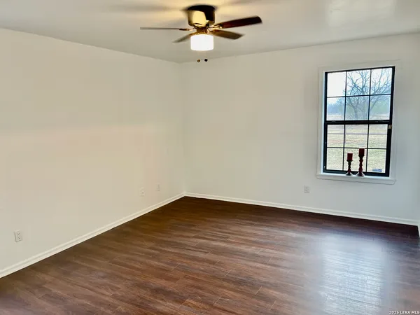 an empty room with wooden floor chandelier fan and windows