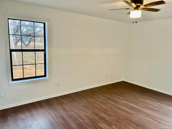 an empty room with wooden floor fan and windows