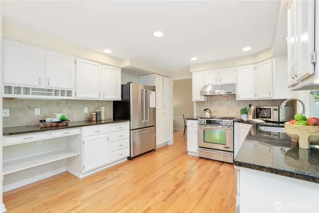 a kitchen with granite countertop a refrigerator stove a sink and dishwasher with wooden floor