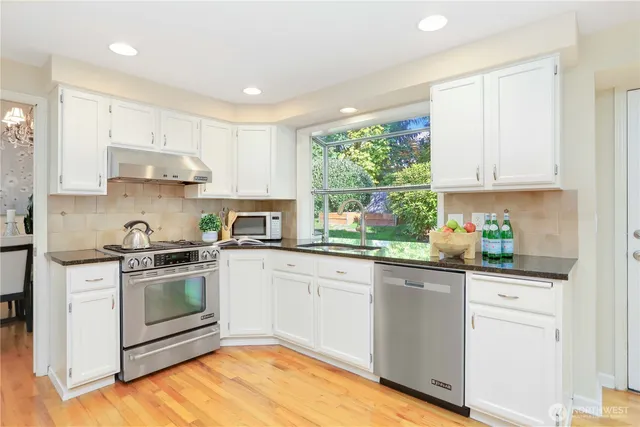 a kitchen with stainless steel appliances granite countertop a stove a sink and white cabinets