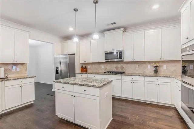 a kitchen with stainless steel appliances granite countertop a sink a stove a refrigerator and white cabinets