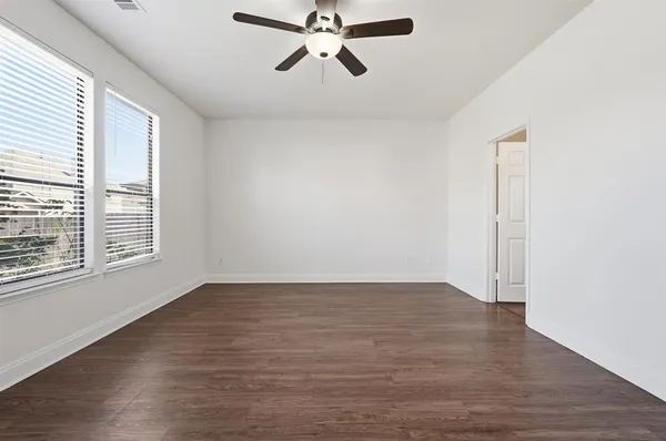 an empty room with wooden floor fan and windows