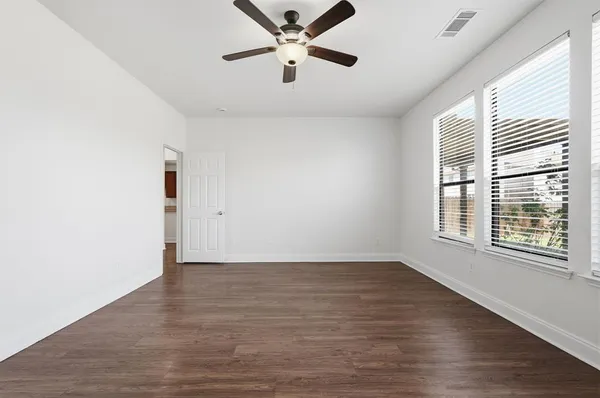 an empty room with wooden floor fan and windows