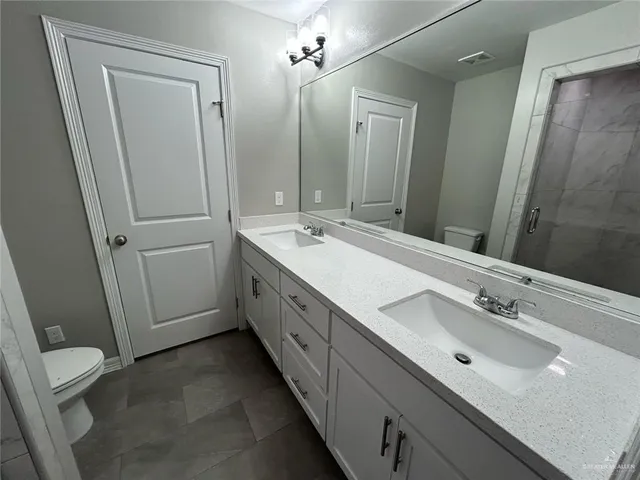 a spacious bathroom with a double vanity sink a toilet and a mirror