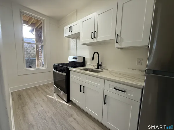 a kitchen with stainless steel appliances a sink a stove a refrigerator a window and cabinets