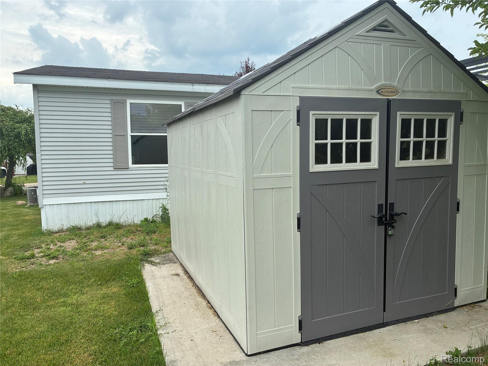 7364 Kings Court Alma, MI 48801 - Photo 2 of 16 Freestanding storage shed with paneled double doors featuring window accents and dark hardware, set on a concrete pad