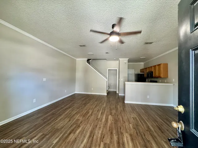 an empty room with wooden floor a kitchen view and windows