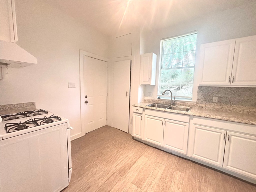 2410 East 12th Street Austin, TX 78702 - Photo 13 of 17 Kitchen with white gas range oven, light wood finished floors, white cabinets, exhaust hood, and decorative backsplash