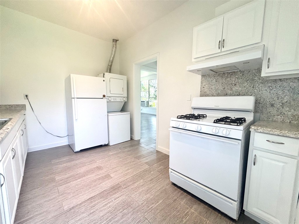 2410 East 12th Street Austin, TX 78702 - Photo 14 of 17 Kitchen with stacked washer and clothes dryer, white appliances, under cabinet range hood, tasteful backsplash, and light wood-type flooring