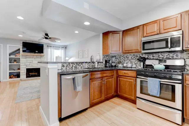 a kitchen with stainless steel appliances granite countertop a stove top oven a sink dishwasher a refrigerator and a fireplace with wooden floor