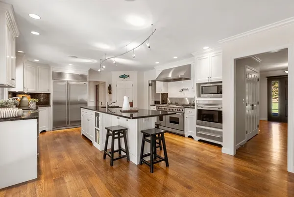 a kitchen with stainless steel appliances kitchen island wooden floors refrigerator stove and white cabinets
