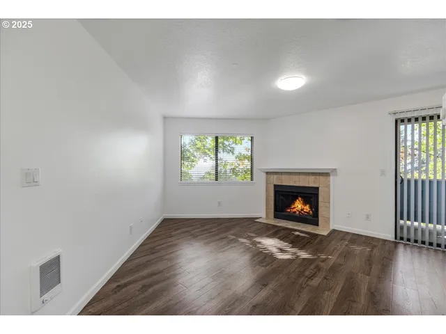 a view of an empty room with wooden floor fireplace and a window
