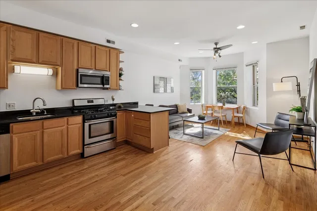 a kitchen with stainless steel appliances a stove a sink a refrigerator wooden floor cabinets and a dining table