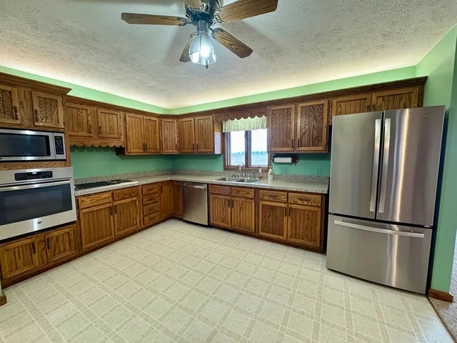 a kitchen with stainless steel appliances granite countertop a refrigerator a sink dishwasher a stove with wooden cabinets and floor