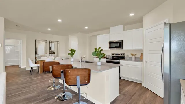 a kitchen with stainless steel appliances granite countertop a refrigerator a stove a sink dishwasher and a dining table with wooden floor