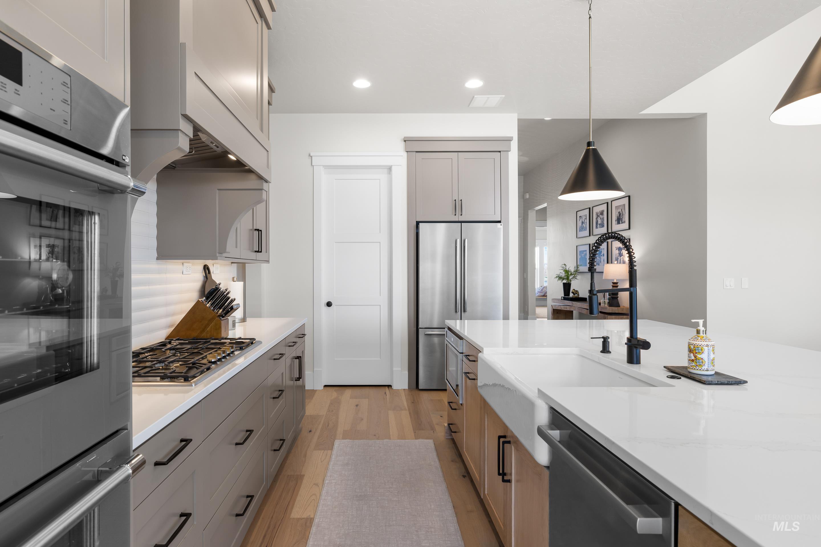 4217 North Bryant Way Meridian, ID 83646 - Photo 11 of 46 Kitchen with stainless steel appliances, light wood-style floors, decorative light fixtures, gray cabinetry, and light stone counters