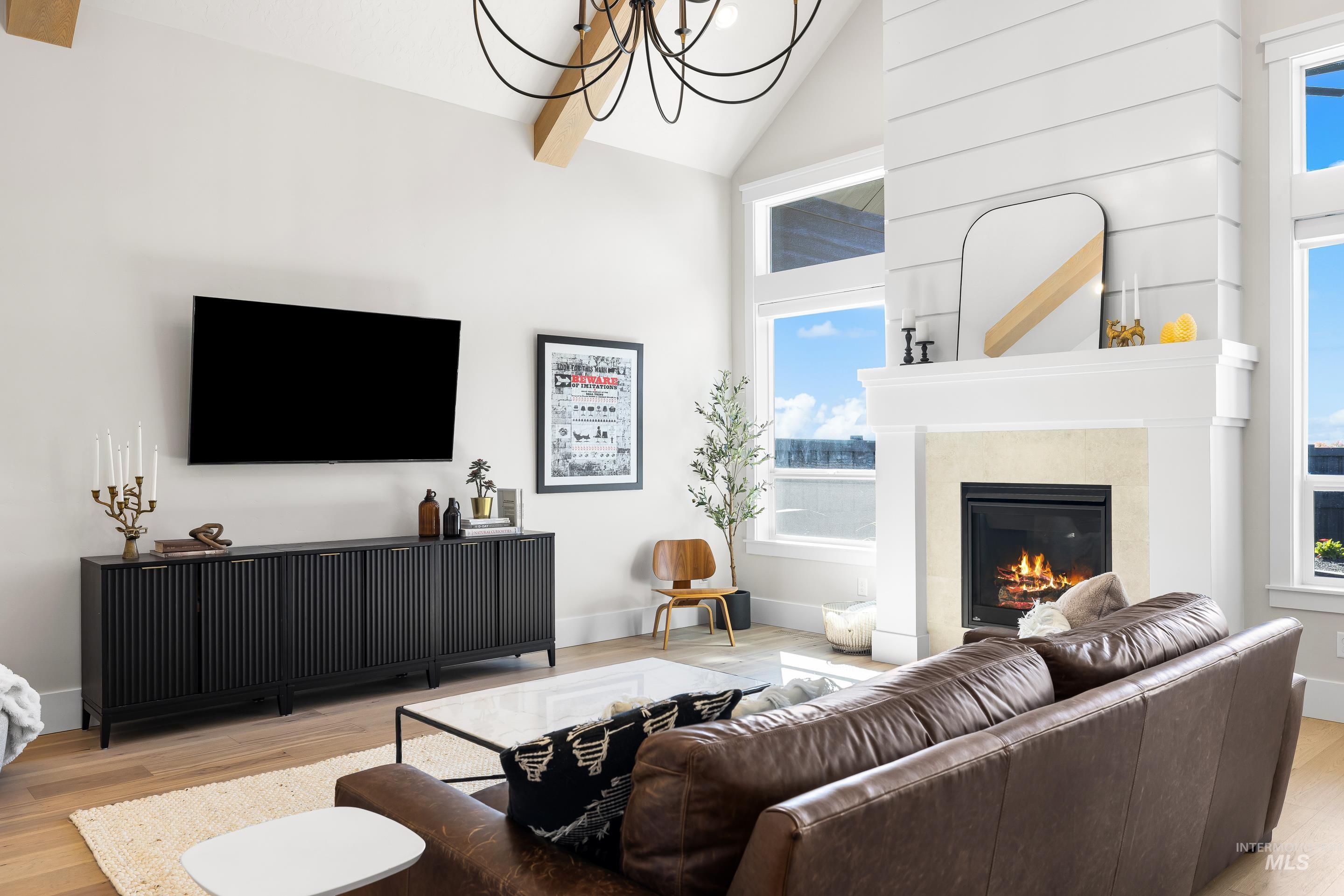 4217 North Bryant Way Meridian, ID 83646 - Photo 14 of 46 Living area with light wood-style flooring, a glass covered fireplace, high vaulted ceiling, a chandelier, and beam ceiling