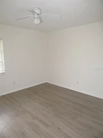 a view of an empty room with wooden floor and a ceiling fan