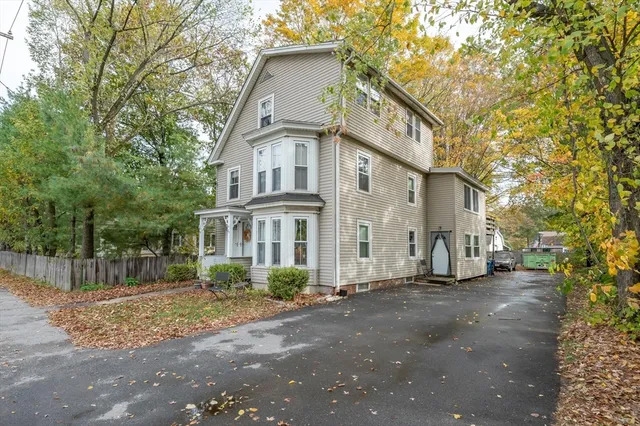 a view of a white house next to a road with large trees