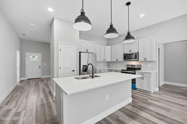 a open kitchen with stainless steel appliances granite countertop a sink a stove a refrigerator and white cabinets with wooden floor