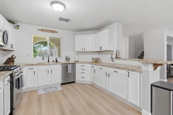 a kitchen with granite countertop white cabinets a sink a window and stainless steel appliances