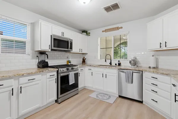 a kitchen with stainless steel appliances granite countertop white cabinets a sink a stove a microwave and wooden floors