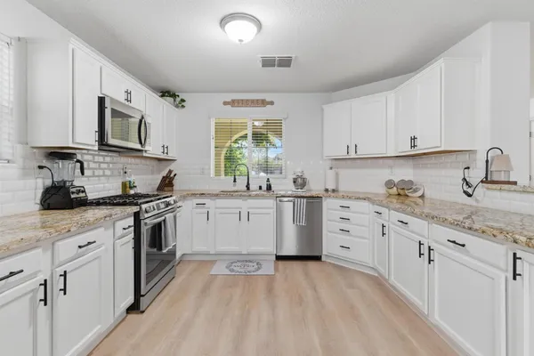 a kitchen with granite countertop white cabinets sink and stainless steel appliances