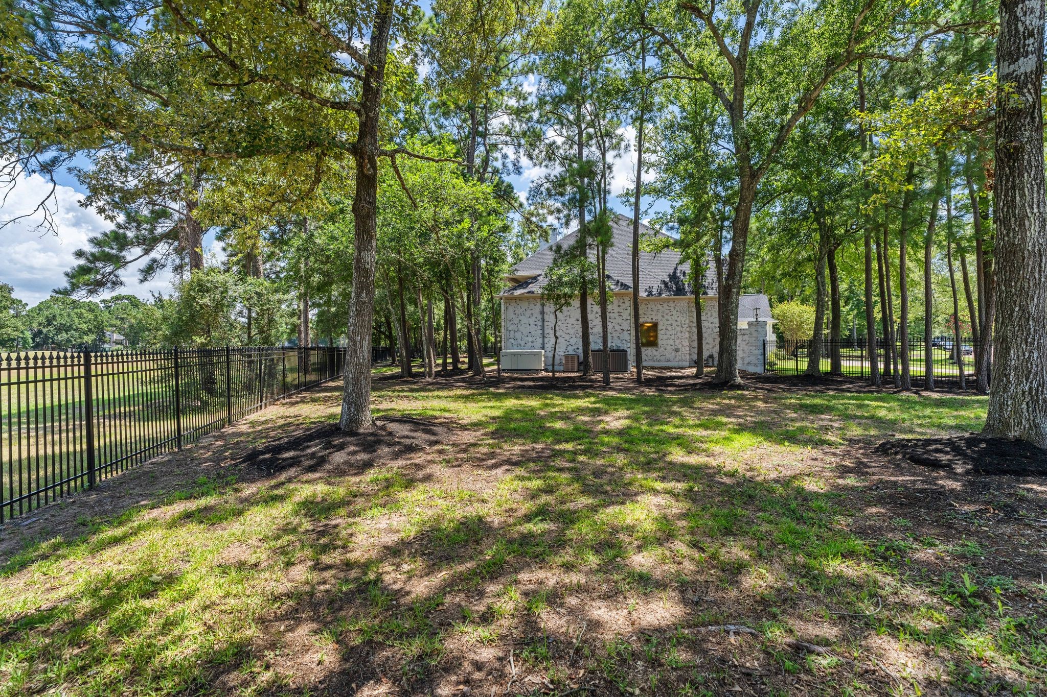 31 Hollymead Drive Spring, TX 77381 - Photo 46 of 50 This photo showcases a spacious, tree-lined backyard with a wrought iron fence, providing a serene and private outdoor space. The house is surrounded by mature trees, offering a natural and tranquil setting. it provides a gate to the golf course cart path.