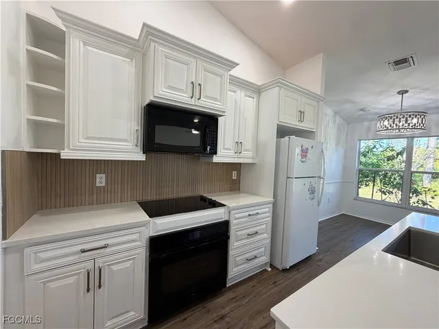 a kitchen with stainless steel appliances granite countertop a refrigerator a stove a sink and white cabinets with wooden floor