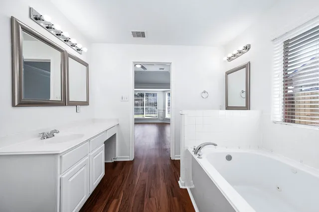 a bathroom with a bathtub a sink a mirror a vanity and window