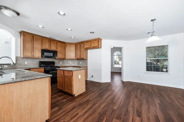 a kitchen with granite countertop wooden floors a stove a sink and a white refrigerator