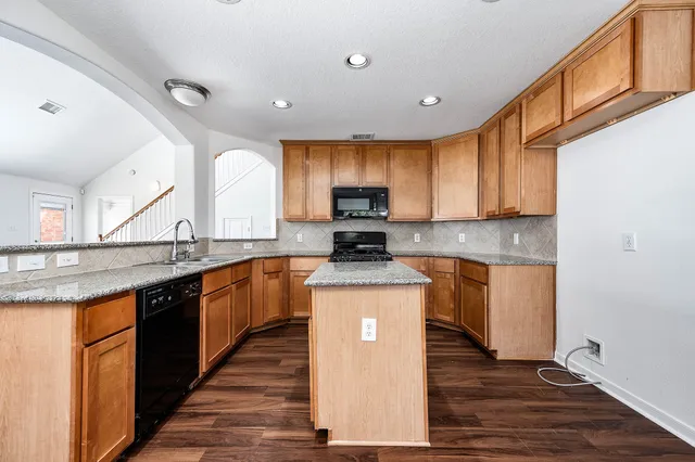 a kitchen with stainless steel appliances granite countertop wooden cabinets a sink and dishwasher a stove top oven with wooden floor