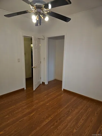 a view of an empty room with wooden floor and a ceiling fan