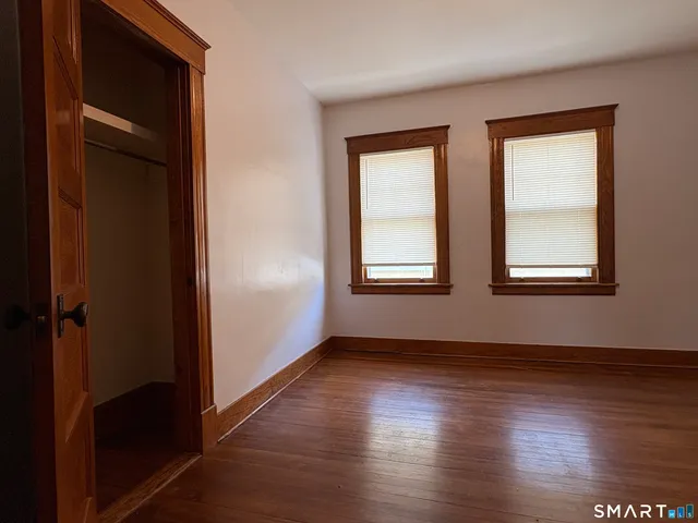 an empty room with wooden floor closet and windows