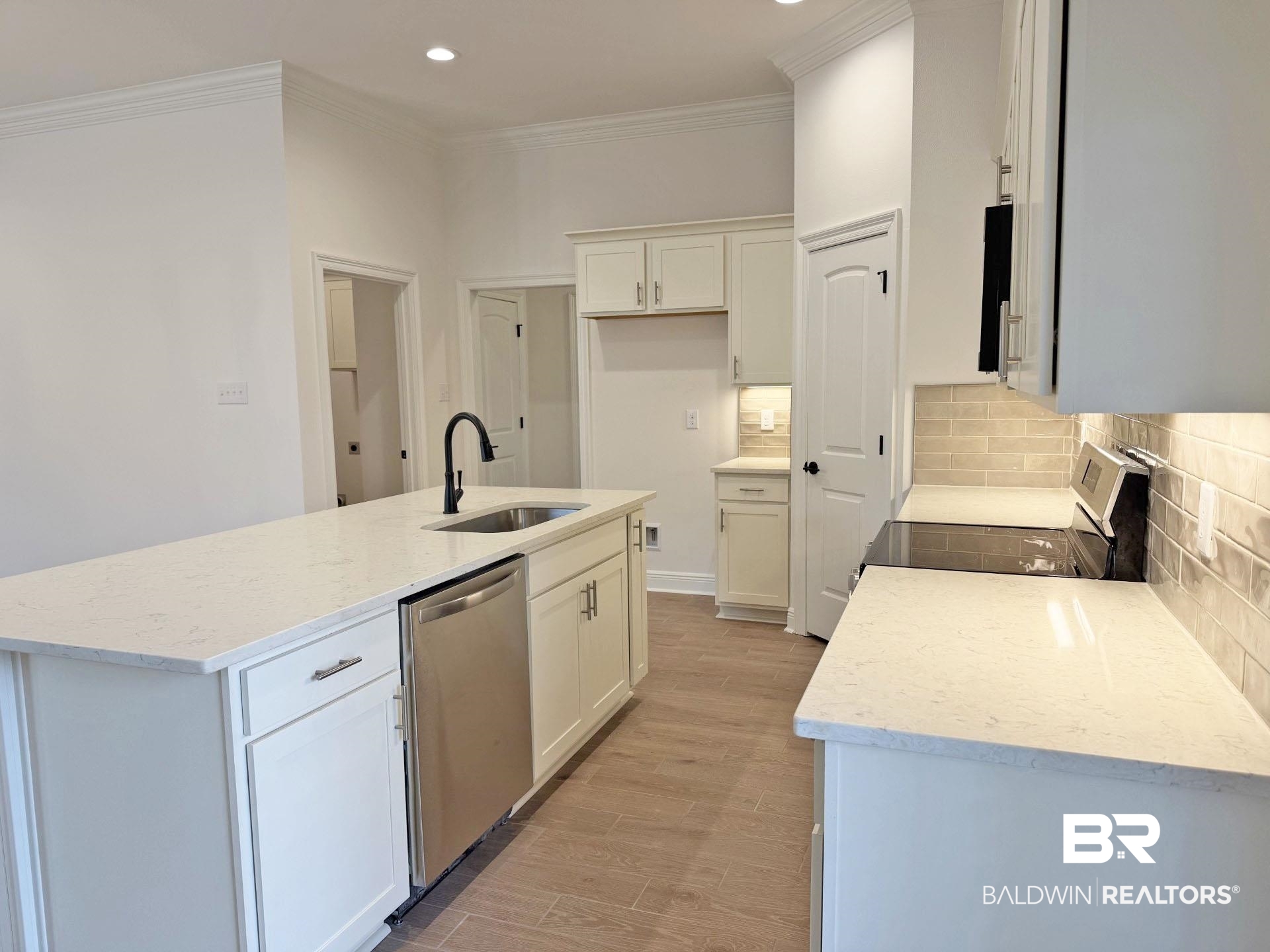 1753 Breckinridge Place Foley, AL 36535 - Photo 5 of 24 Contemporary kitchen featuring a large island with an undermount sink, a stainless steel dishwasher, white shaker cabinetry with brushed nickel hardware, light-toned countertops, and a subway tile backsplash
