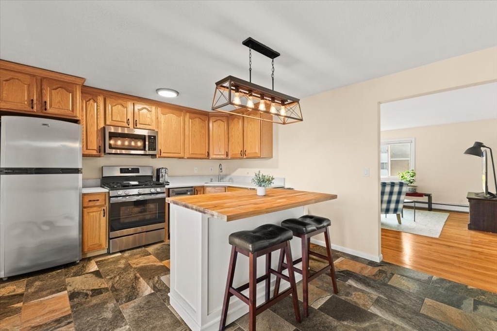 39 Will Drive, Unit 16 Canton, MA 02021 - Photo 2 of 13 a kitchen with stainless steel appliances granite countertop a stove top oven a sink a dining table and chairs with wooden floor