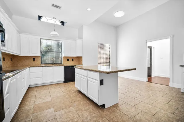 a large kitchen with stainless steel appliances kitchen island granite countertop a stove a sink and white cabinets
